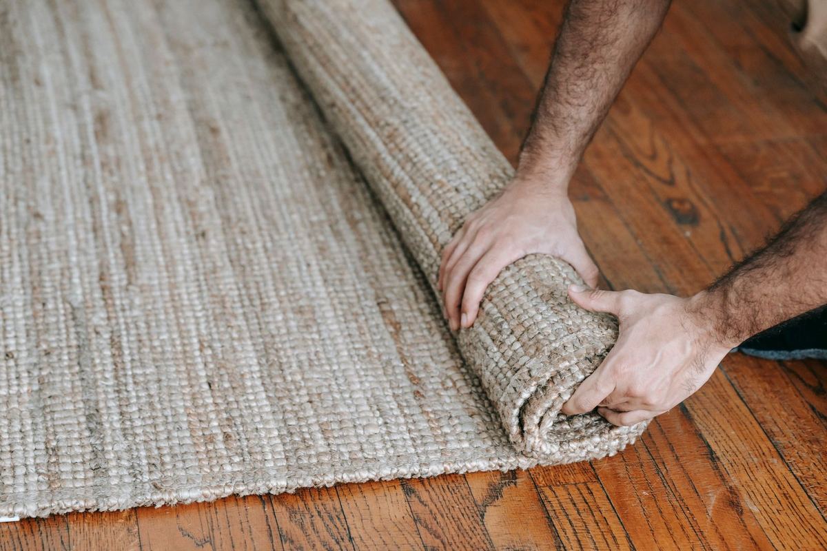 Hands rolling up a woven area rug on a wood floor